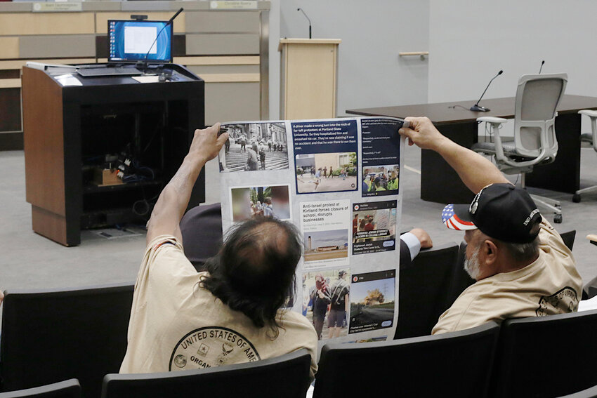 Two residents look at a poster of printed-out headlines, a prop for use during public comments at the Las Cruces City Council meeting on May 6, 2024.