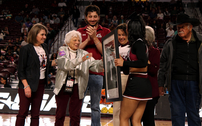 Barbara Hubbard receiving a jersey gifted by the New Mexico State Women’s basketball program from a New Mexico State cheerleader while flanked by Amber Burdge, Marci Dickerson and the family of Sybil Dickerson Clagett.