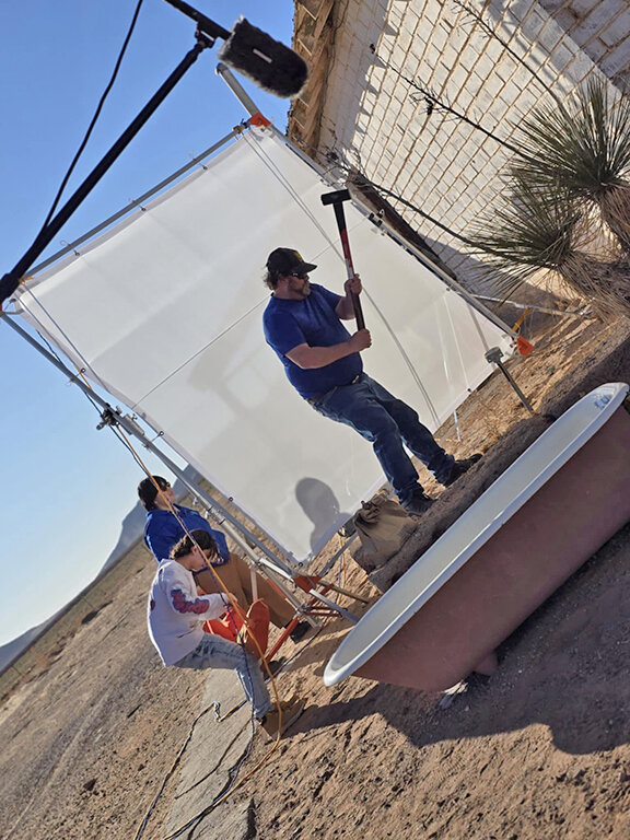 Instructor Dan Williams drives a stake to teach students how to safely tie off an overhead diffusion frame in southwestern winds.