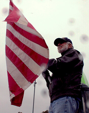 Patrick Stafford stands with an upside-down American flag at the Hands Off! Protest on April 5, 2025. A nationwide protest to oppose President Trump’s recent executive orders and policy changes implemented by the Department of Government Efficiency.