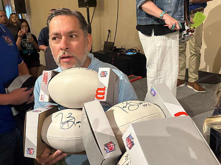Mark Figueroa, owner of Del Valle Physical Therapy & Hand Therapy, excitedly gathers the four autographed footballs he purchased as part of the fundraising