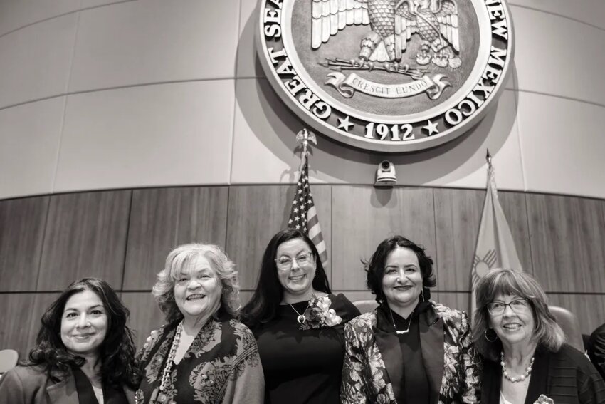 From left: Kristina Ortez, Susan Herrera, Katy Duhigg, Angelica Rubio and Joy Garratt in front of the Seal of the State of New Mexico on the House floor in the Roundhouse.