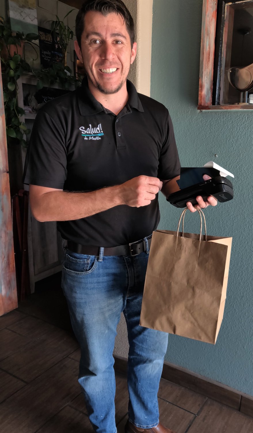 Russell Hernandez, co-owner of Salud! de Mesilla, hands an eco-friendly brown, paper bag to a customer who ordered ahead. Salud! and other restaurants are making to-go orders sustainable during the COVID-19 transition.