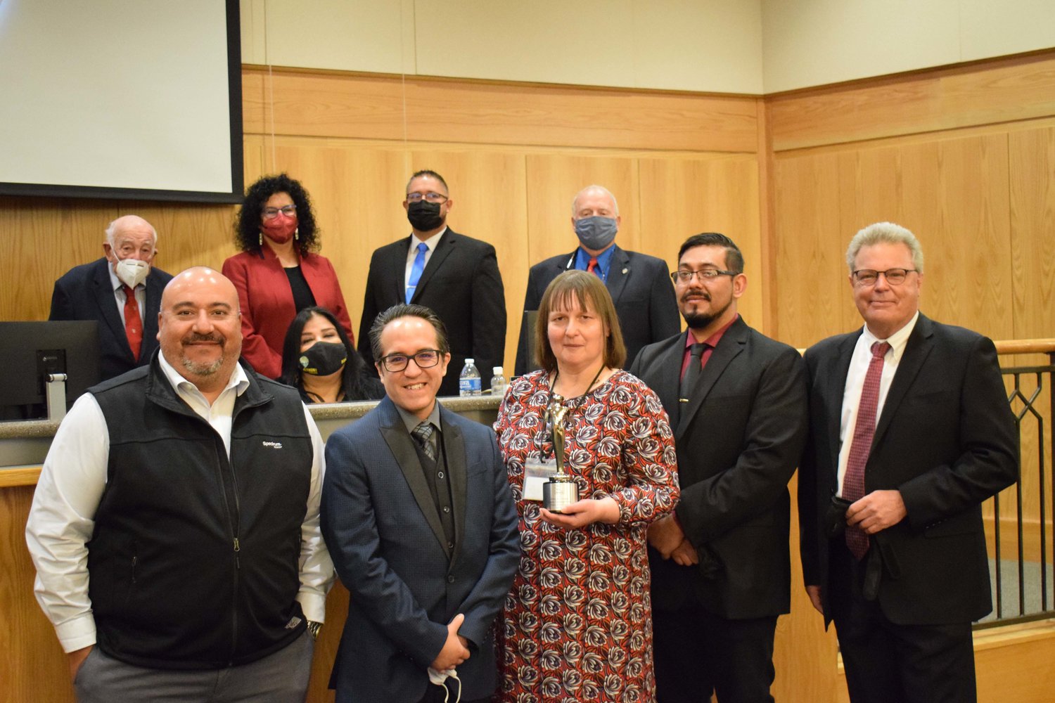 Receiving a 2021 Silver Telly Award for Doña Ana County, are, left to right, Al Marquez and Joel Marquez, both of Spectrum Reach; county Community and Constituent Services Manager Liz Reed; county Public Information Office Multi-Media Coordinator Joseph Vargas; and Spectrum Reach local Sales Manager Ray May. Behind the dais are, Doña Ana County Commissioners, standing, left to right, Lynn Ellins, Susie Chaparro, Manuel Sanchez and Shannon Reynolds; and, seated, Diana Murillo-Trujillo