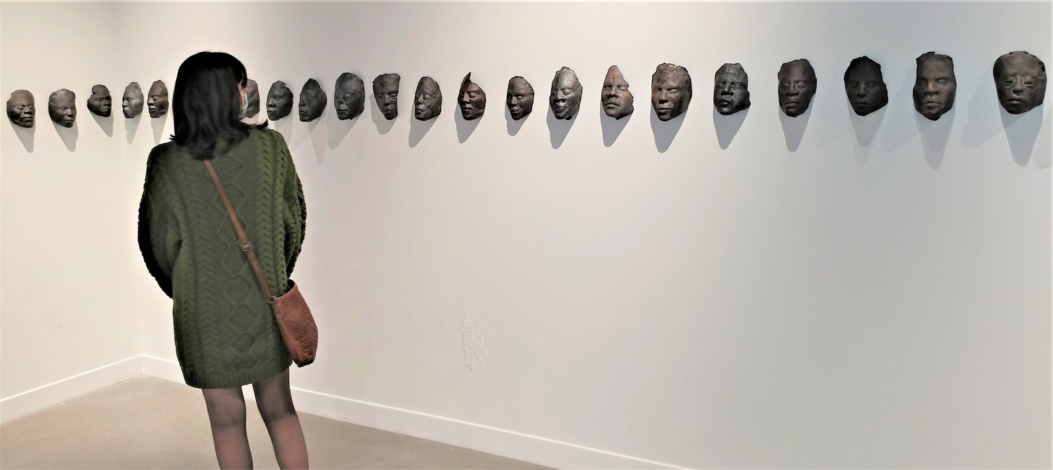 A visitor to the exhibitions that opened Jan. 21 at the NMSU Art Museum takes in “Death Masks,” “a large-scale ceramic installation centered on the living experience of shared wounds,” said Nikesha Breeze, the artist who created them.