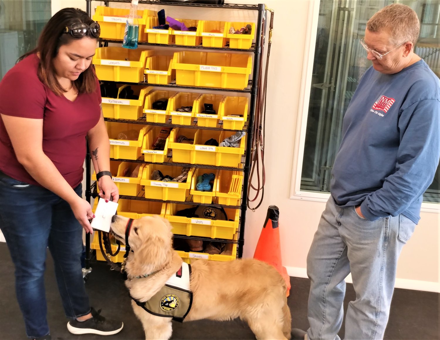 As Four Paws and a Wake Up, Inc. owner Andrea Joseph looks on, trainer Aly De La O helps CB get to know what a light switch feels and smells like. The large windows in back will allow dogs in kennels to watch and learn as other dogs are trained.