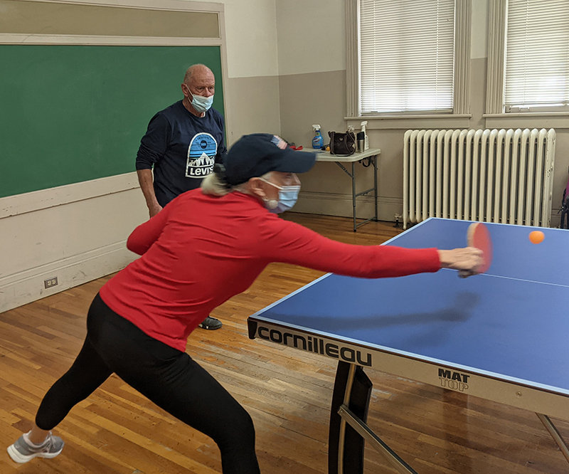 Susan Gutierrez stays active and fit by playing the low-impact sport of table tennis. Here she reaches for that ever-bouncing orange ball while doubles partner Ernst Bolleter looks on.