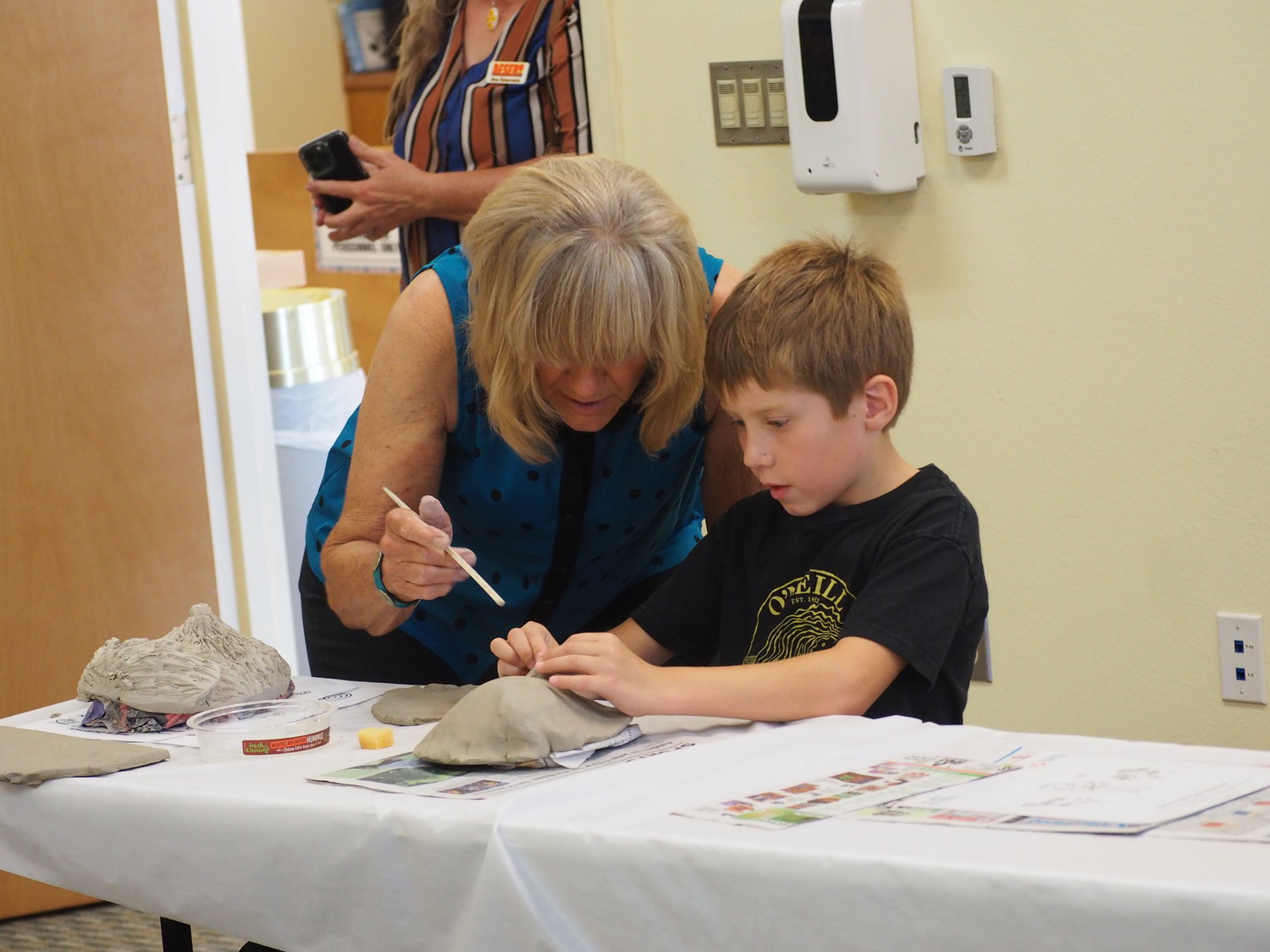 A CLAY Festival volunteer works with a student molding a clay mask in the Bayard Public Library.