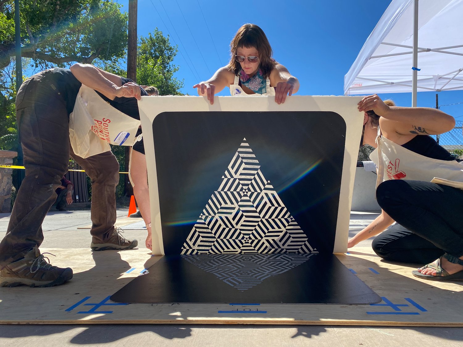 Alyssa Bell, the volunteer in the middle of the photo, and other volunteers are printing a piece by Daniel Garver, from Silver City, during the Southwest Print Fiesta steamroller printing event during the 2021 event.