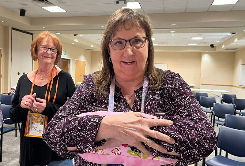 Guild member Jennifer Terrazas demonstrates some of the ways the pillows made for breast cancer patients by Las Colcheras Quilt Guilds can be used. Behind her is another guild member, Gail Carney.