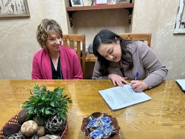 CEO Ashley Echavarria signs closing documents for the purchase of the former Video 4 cinema on El Paso Road, while Vice-Chair of the Board of Directors Valerie Pickett watches.
