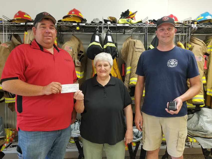 Firemen, Derek Weckerling (L) and Travis Thomforde accept a check from Carol Voth, treasurer of the St. Peter's Ladies' Aid.  The money was raised at the Volksfest burrito breakfast and will be used to buy pagers for the firefighters.