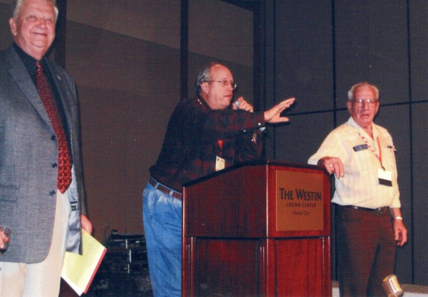 In this 2005 picture on the far right is Cliff Mitchell, KASM radio who was helping with a farm broadcasting benefit auction in Kansas City. On the far left is Orion Samuelson, emcee for the event.  In the middle is Col Jon Phillips, farm broadcast partner of Emery for many years in Iowa and Nebraska.