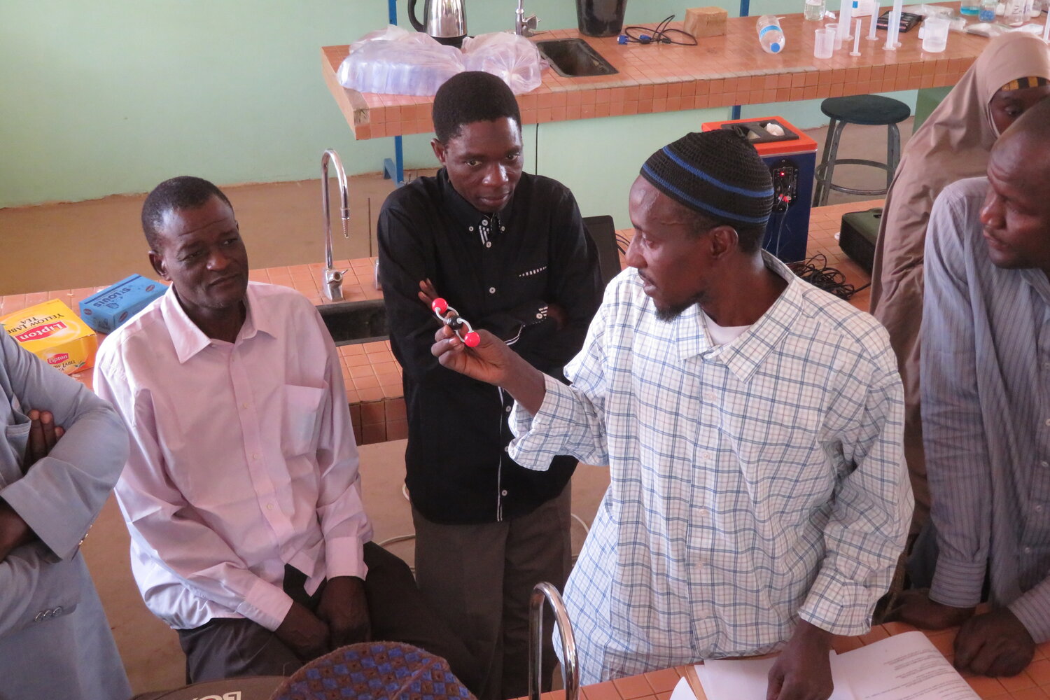 A teacher uses parts of a molecular model kit to illustrate the linear structure and two double bonds characteristic of a molecule of carbon dioxide. Such structural information will help these teachers to explain why carbon is a green-house gas.&nbsp; Photo from 2023 workshops in Niger.