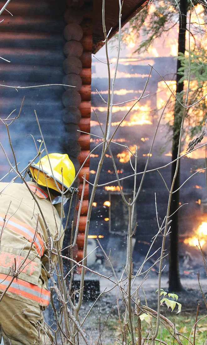 A firefighter from Greenwood Township battles flames at a house fire Wednesday morning.