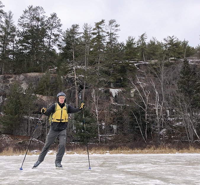 Nordic skating across Nina Moose Lake with a pine-covered bluff in the background.